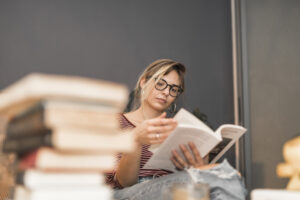 Mulher escritora lendo um livro com pilha de livros sobre a mesa — imagem que representa o universo da autopublicação independente.